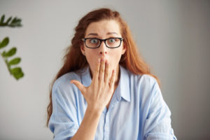 shocked woman covering her mouth surprised to learn the consequences of not brushing teeth
