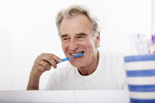 Senior Man In Bathroom Brushing Teeth