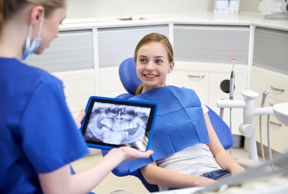 girl patient smiling at dentist with x-ray image on a tablet