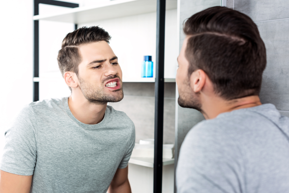 young man looking at his crooked teeth in mirror