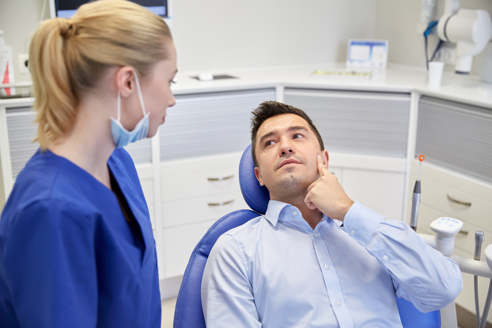 man touching his sore tooth talking to dentist in dental chair