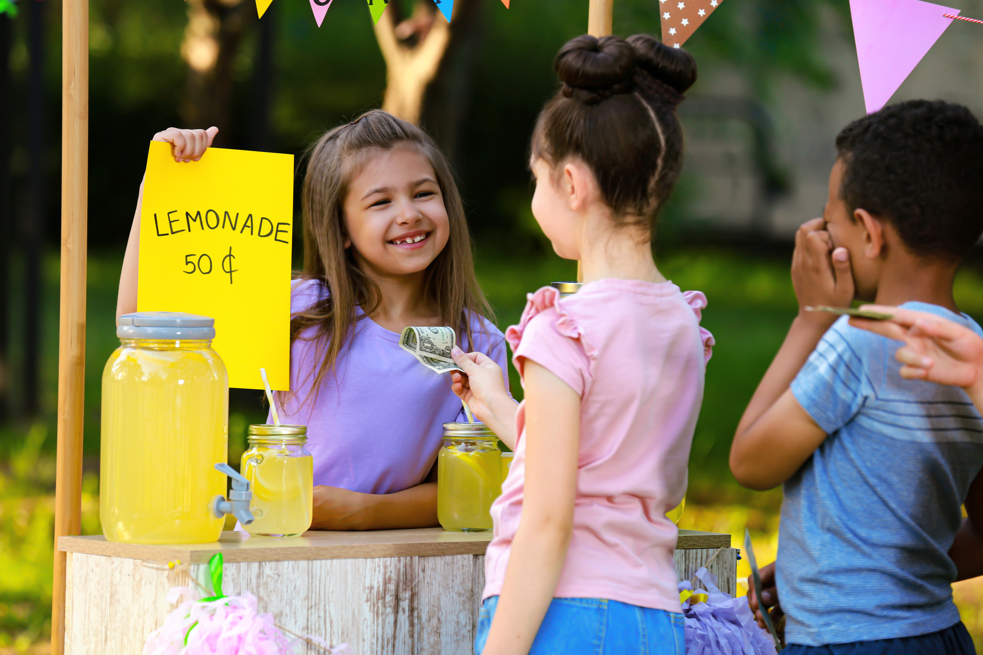 Kids with big smiles having a lemonade stand in the summer.