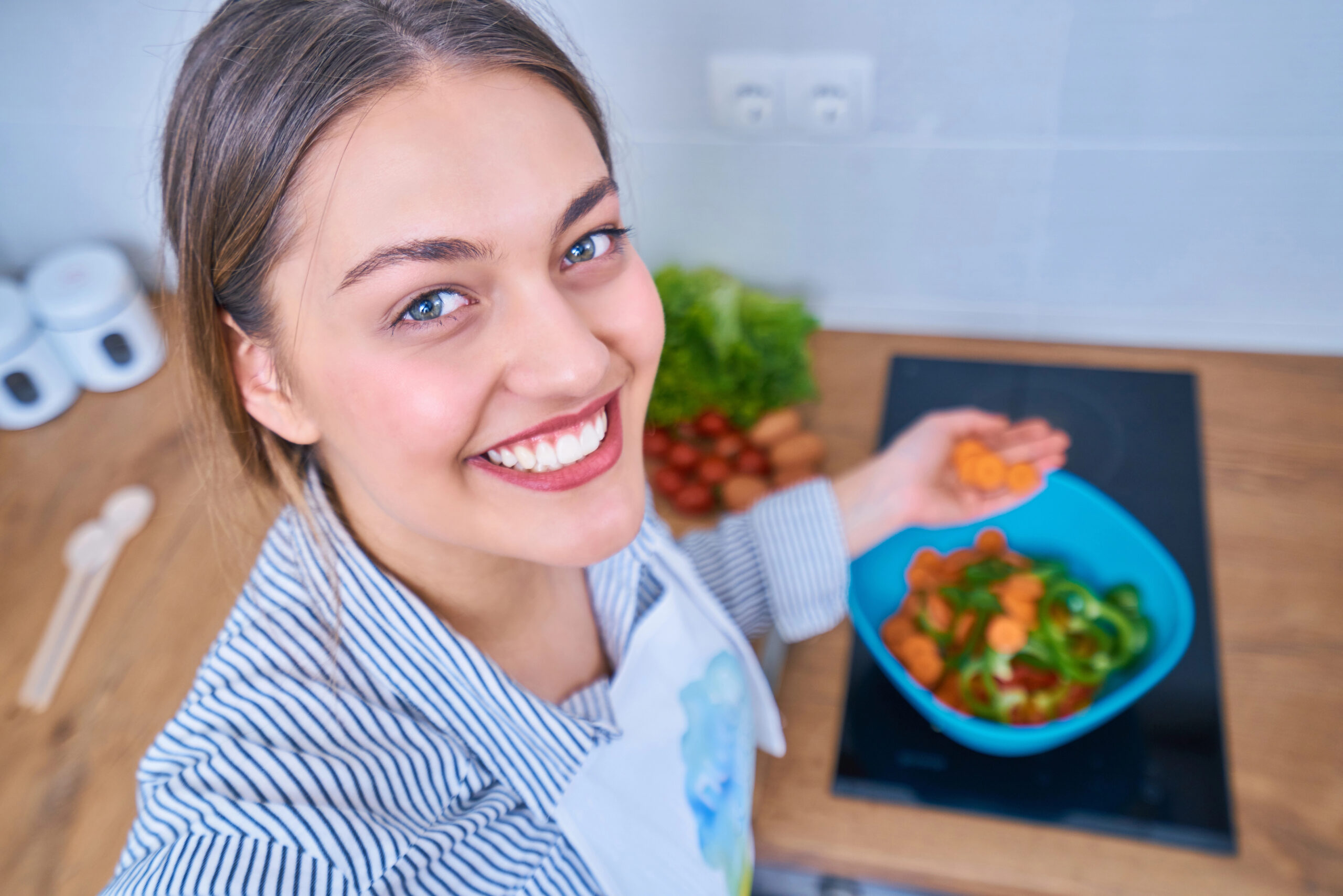 Young woman with healthy white teeth slicing crunchy vegetables.