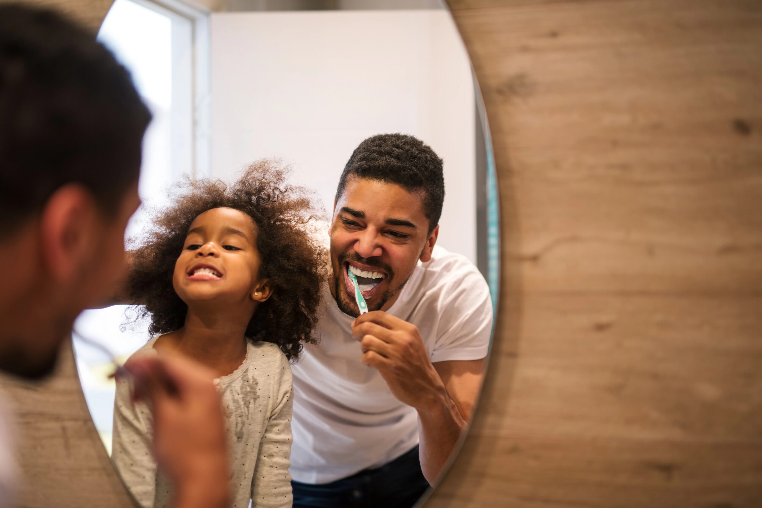 Dad and daughter brushing teeth and laughing together. 