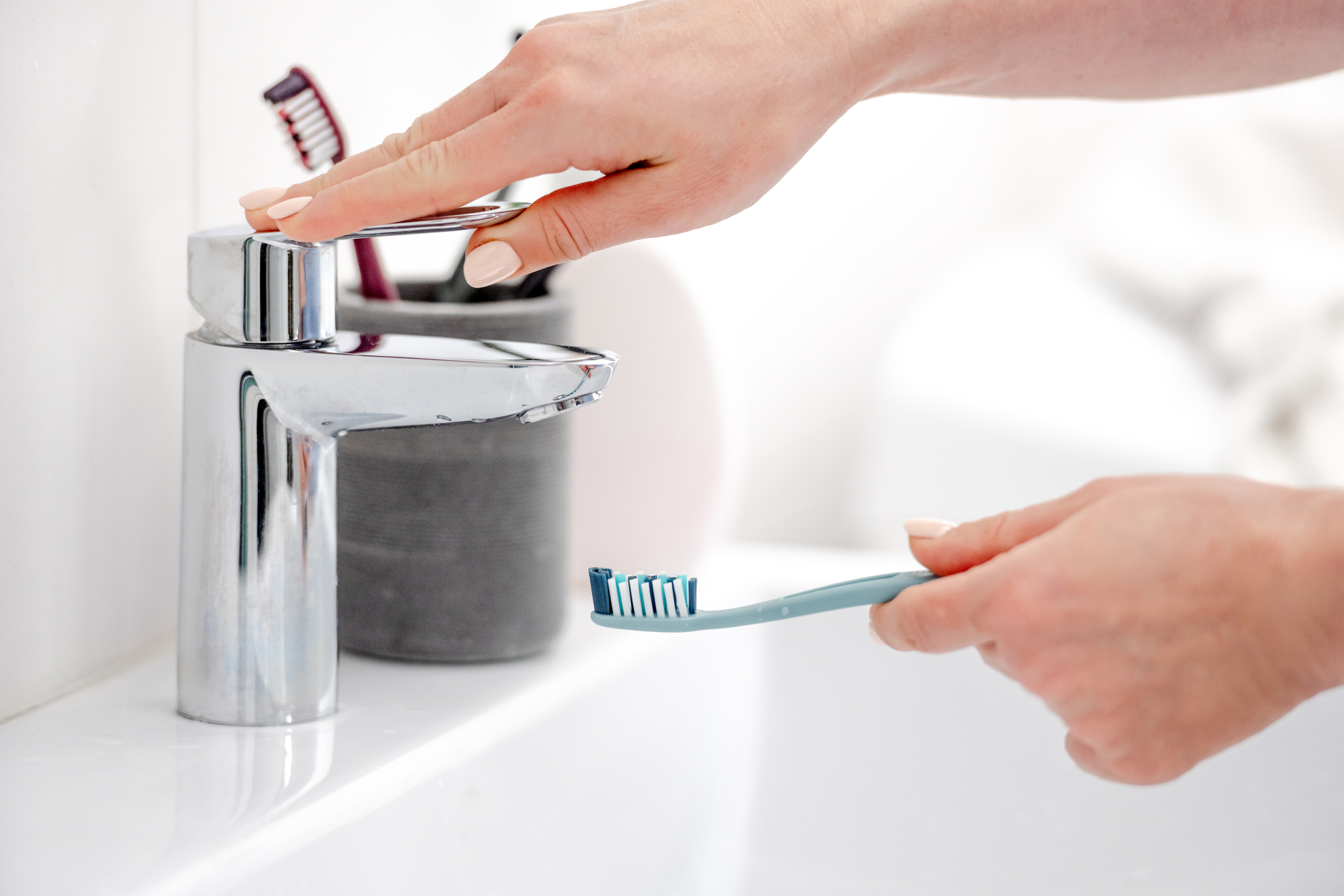 Person's hand rinsing toothbrush in sink. 